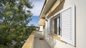 Ein schmaler Außenkorridor mit Fliesenboden, einer Tür mit weißen Fensterläden und einem Streifenmarkisen.