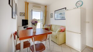 Ein Essbereich mit Tisch und Stühlen, einem Fernseher, einer Couch, einem Kühlschrank und einer Wanduhr.