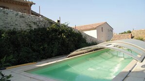 A swimming pool with a curved edge, surrounded by a stone wall and vegetation. - between  carcassonne and narbonne with swimming pool (Capendu)