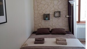 A bedroom with a stone wall, a bed with brown bedding, two pillows, a bedside table, and a lamp. - between  carcassonne and narbonne with swimming pool (Capendu)