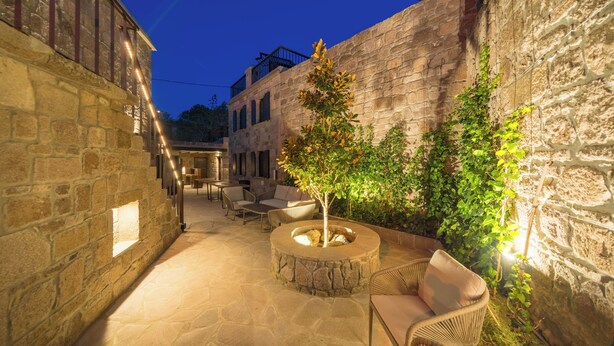 Un espace extérieur aménagé en terrasse, avec des murs en pierre, un coin salon circulaire et un petit arbre.