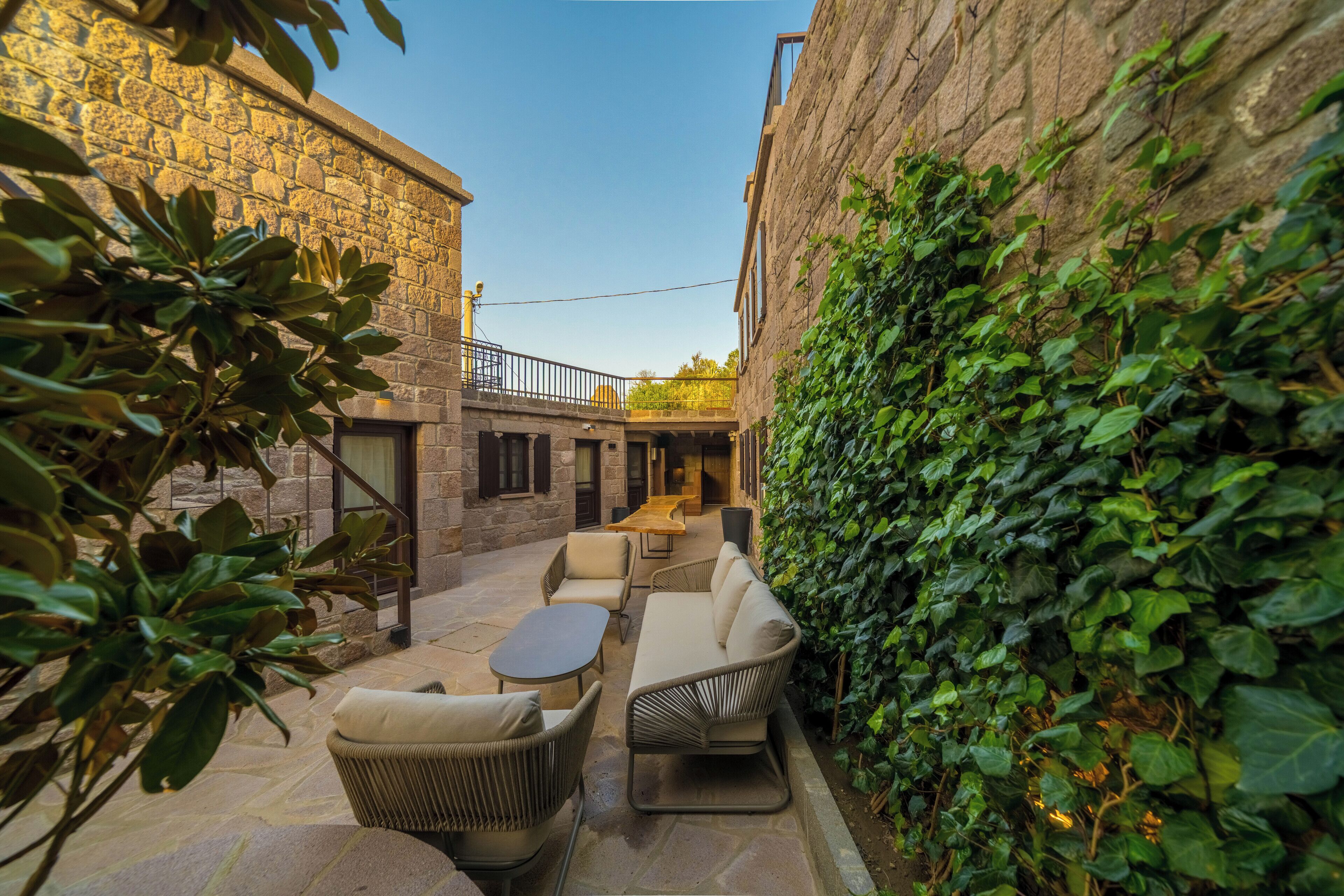 A courtyard with stone walls, a wooden table, and wicker furniture.