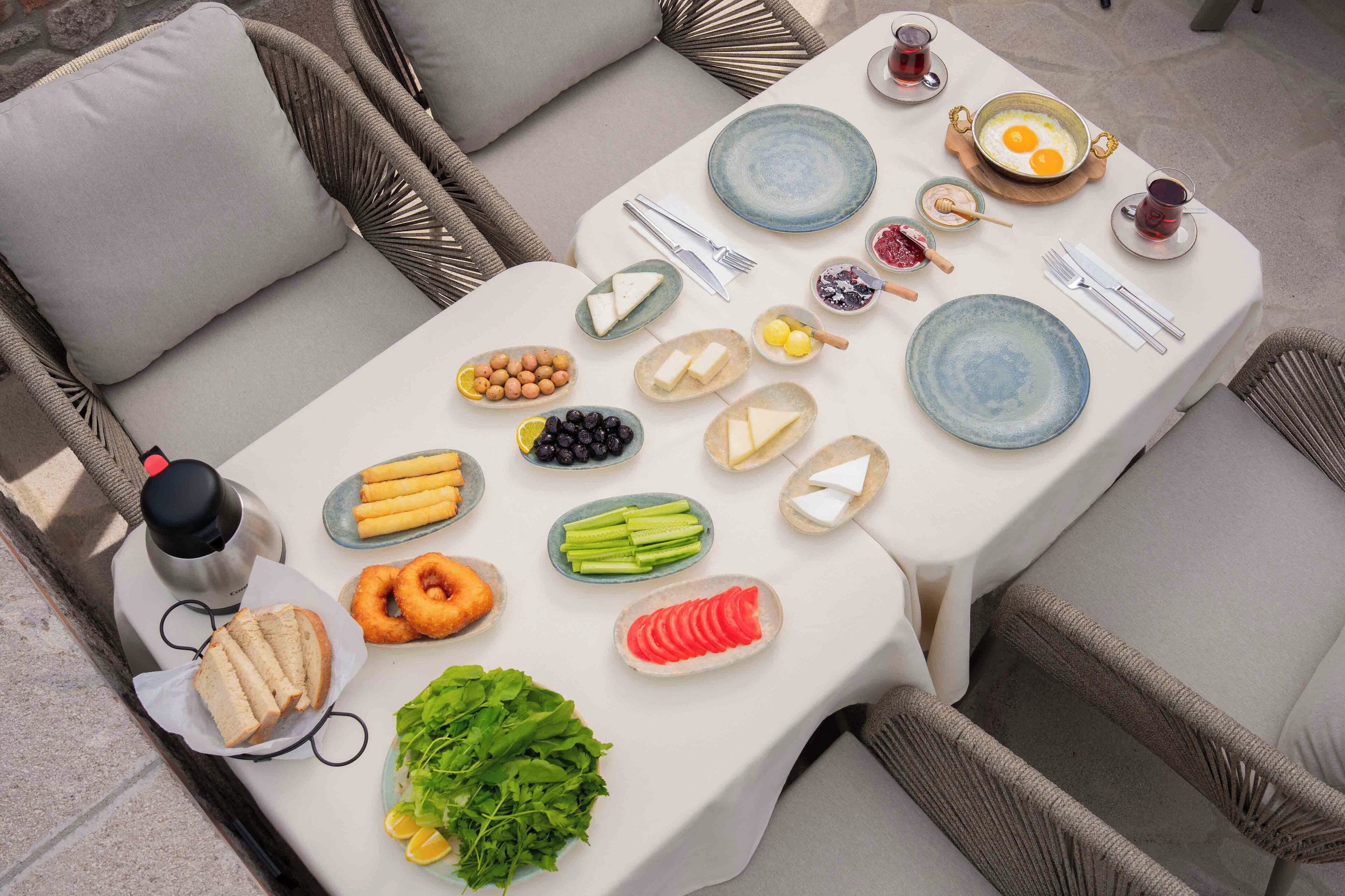 A breakfast table set with various foods, including bread, eggs, cheese, and fruits, on a white tablecloth.