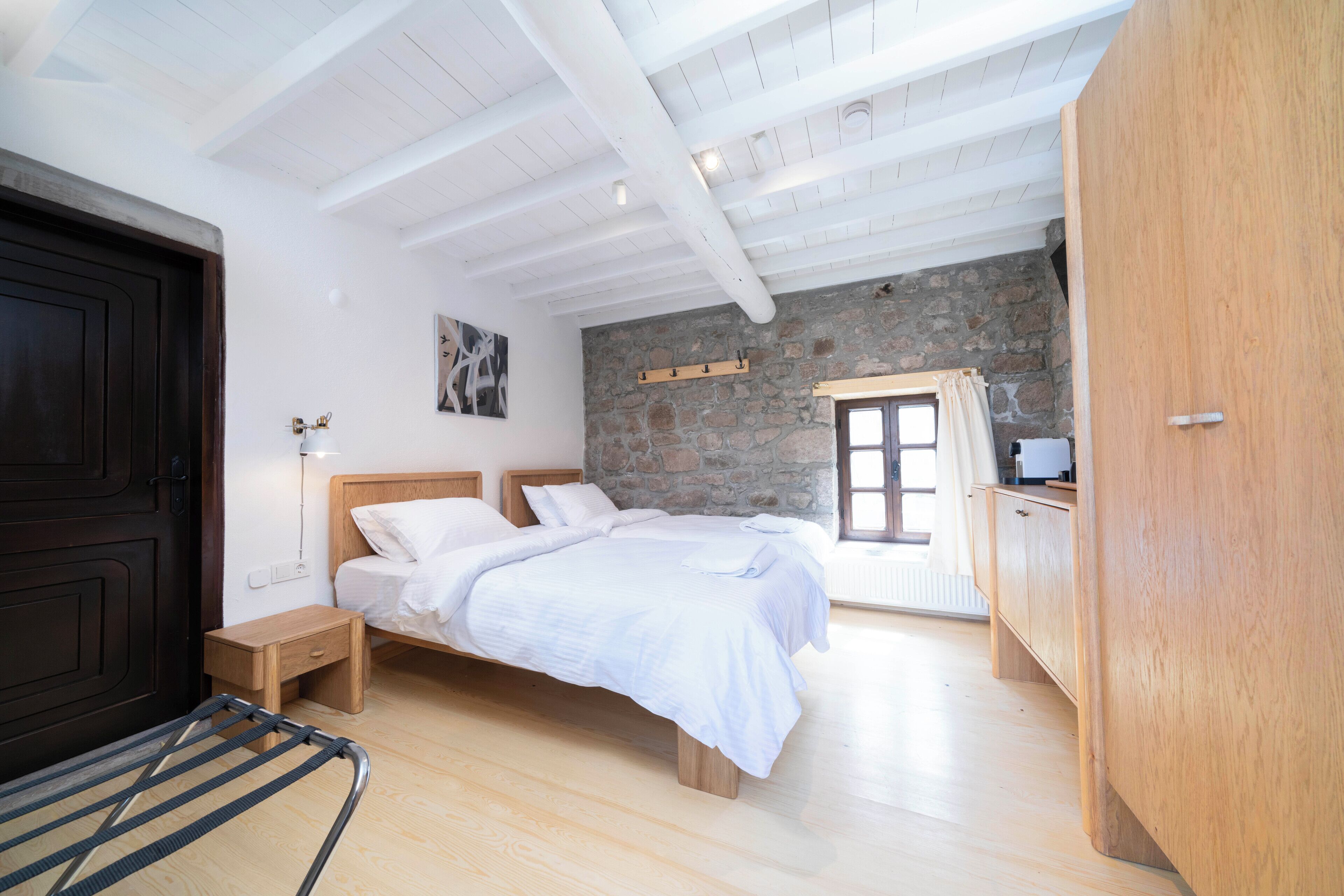 A bedroom with a wooden bed, a small bedside table, a wooden wardrobe, and a stone wall.