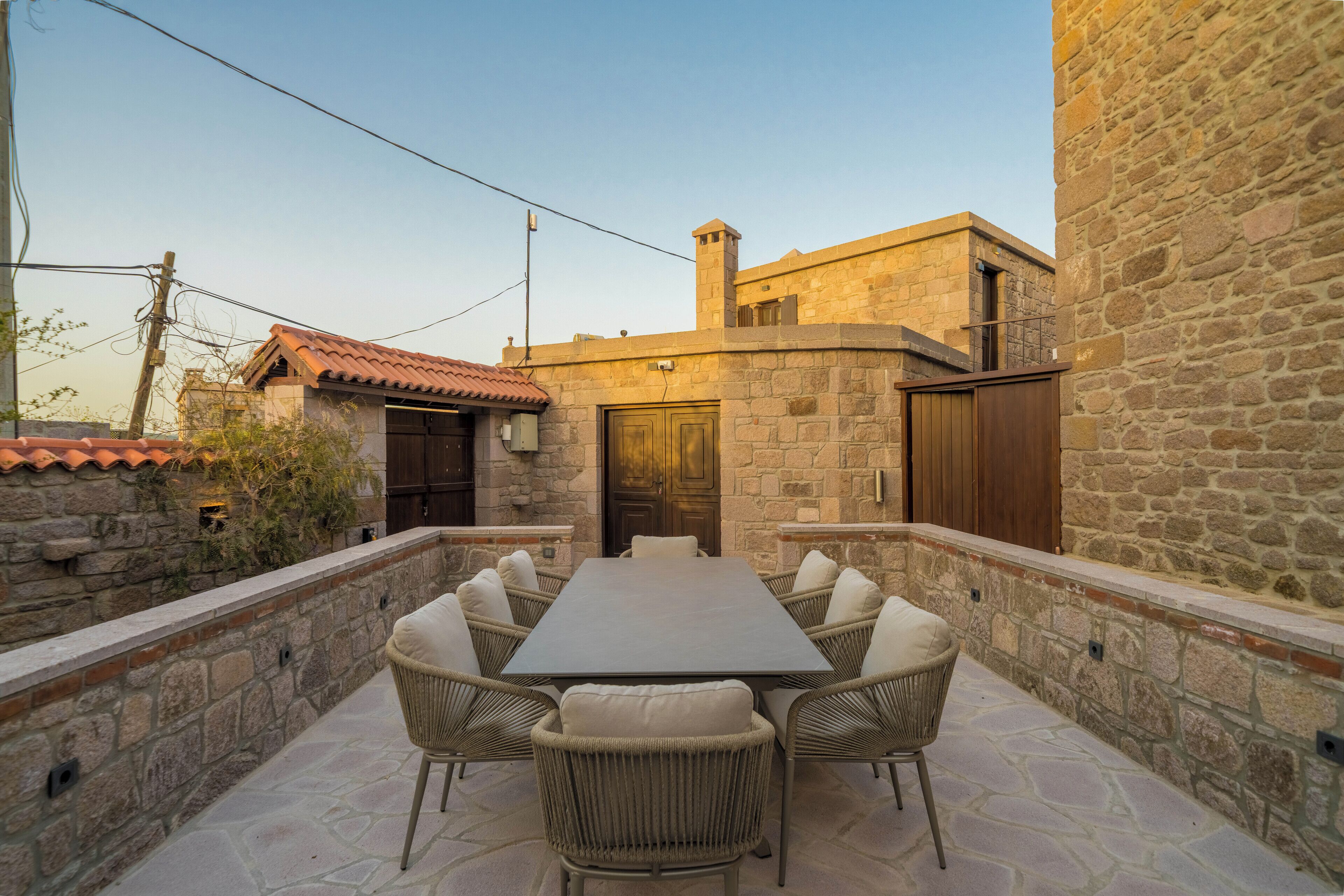 A stone-walled outdoor patio with a rectangular table and wicker chairs.
