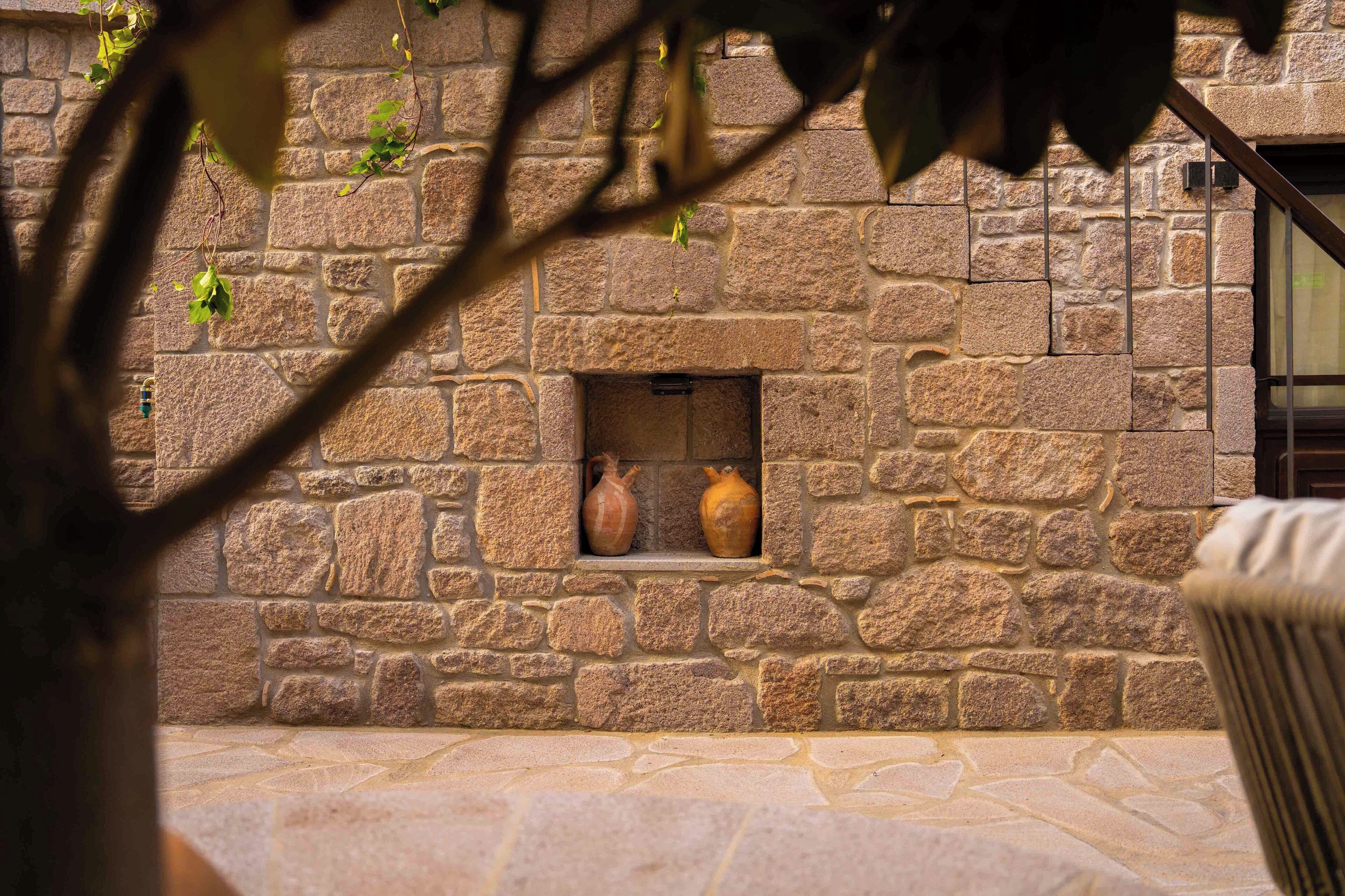 A stone wall with a built-in shelf holding two ceramic pots.