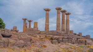 De vieilles colonnes de pierre se dressent sur une colline rocheuse, sous un ciel dégagé.