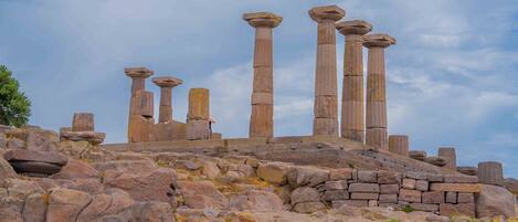 Ancient stone columns on a rocky hill with a clear sky.