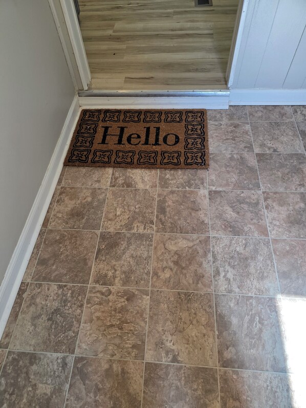 Eine braune Fußmatte mit dem Schriftzug 'Hello' auf gefliestem Boden.