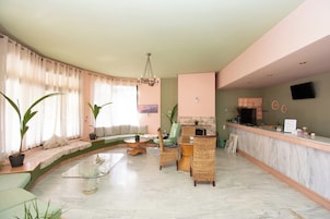 Un salón amplio con un sofá curvo, una mesa de centro de cristal, sillones de mimbre y una recepción de mármol.