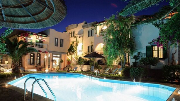 A swimming pool with lounge chairs and a thatched umbrella, surrounded by a building with multiple balconies and plants. - Aquarius Apartments by Checkin (Agia Pelagia)