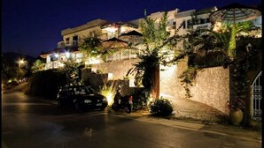A hotel with a stone facade, a paved entrance, and a car parked in front. - Aquarius Apartments by Checkin (Agia Pelagia)