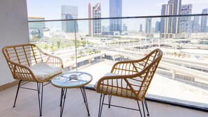 Un balcon agrémenté de fauteuils en osier et d’une table en verre, offrant une vue sur un paysage urbain avec des bâtiments modernes et des autoroutes.