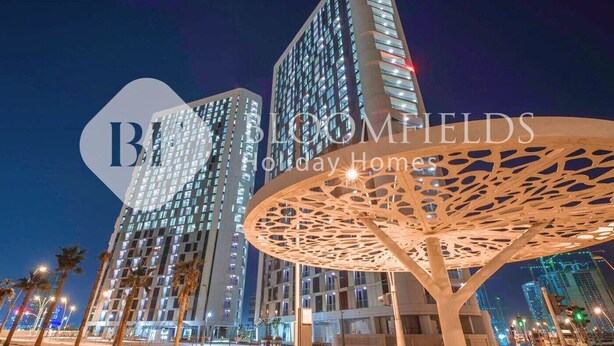 Un hotel moderno con un diseño arquitectónico distintivo, que presenta una gran estructura circular perforada en primer plano y edificios de gran altura al fondo.