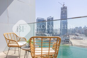 A balcony with wicker chairs and a view of a cityscape and beach. - Bloomfileds Executive Studio In Al Maryah Island (Abu Dabi)