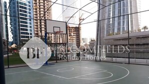 Un terrain de basket avec un panier, entouré de grands immeubles et de chantiers de construction.