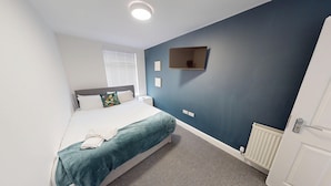 A modern hotel room with a bed, a flat-screen TV mounted on the wall, a bedside table, and a radiator. - For Workers | 10 Mins to City | 5 TVs and Parking (Liverpool)