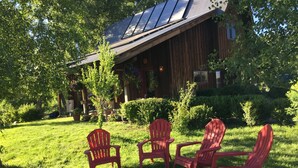 A wooden house with solar panels on the roof, surrounded by a well-maintained lawn and three red Adirondack chairs. - Oso Verde Ranch, a natural oasis, is located just a mile from downtown Mancos (Mancos)