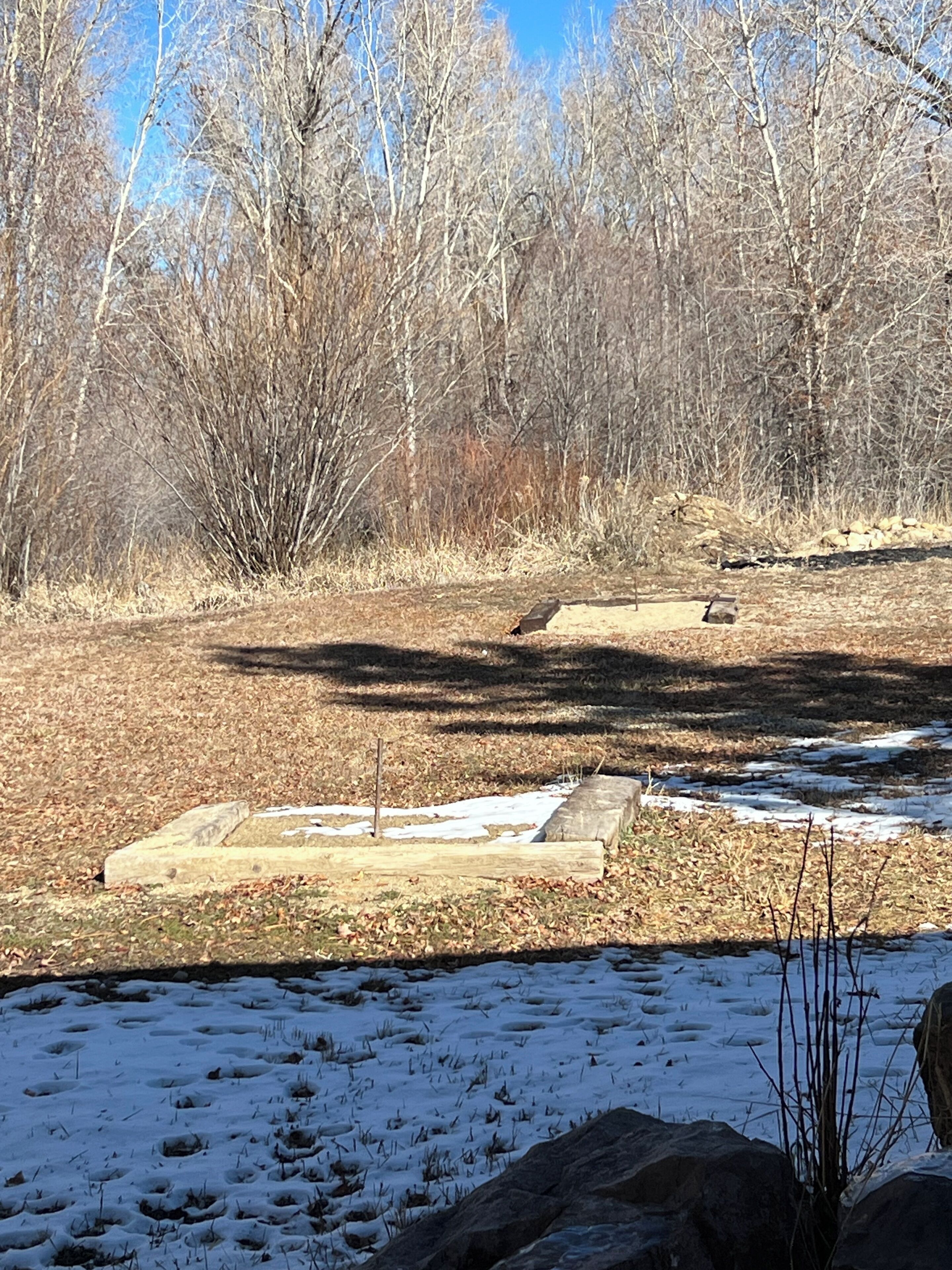 A natural landscape with a stream, snow patches, and leafless trees.
