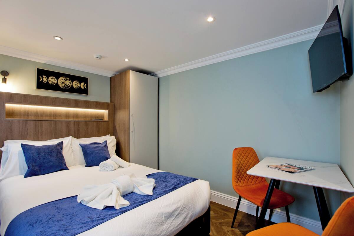 A hotel room with a bed, a small table, and a TV mounted on the wall.