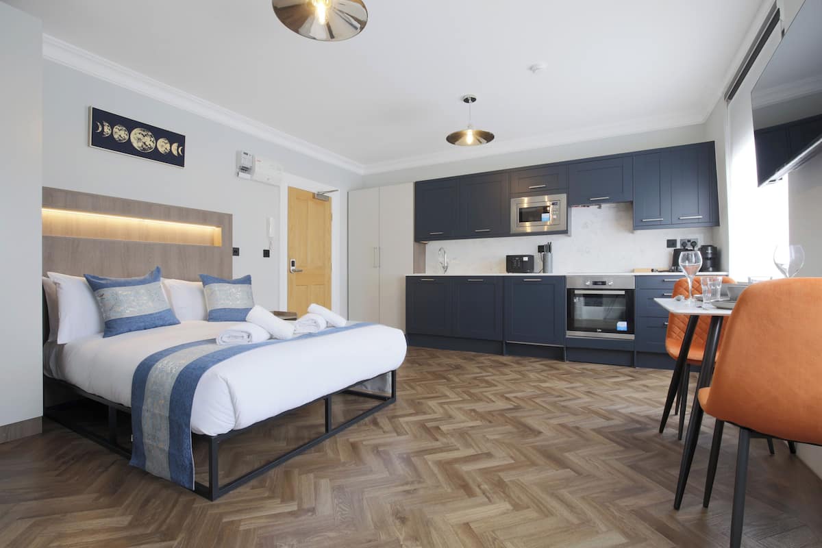 A modern hotel room with a bed, a dining area, and a kitchen.