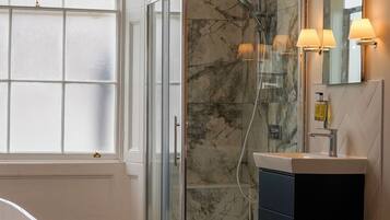 A bathroom with a glass-enclosed shower, a vanity with a mirror, and a window with frosted glass panels.