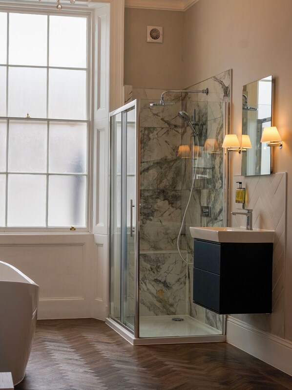 A bathroom with a glass-enclosed shower, a vanity with a mirror, and a window with frosted glass panels. - Imperial York Street Apartments (London)