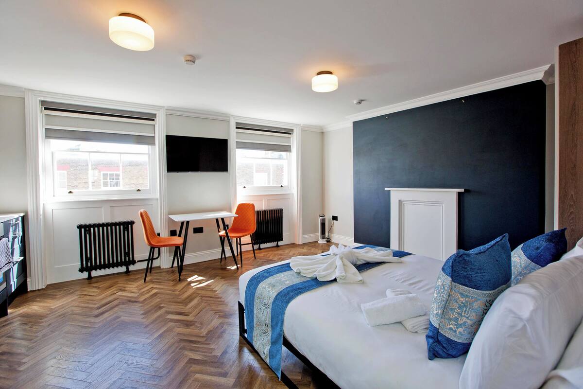 A hotel room with a large bed, a desk, an orange chair, and a TV mounted on the wall.