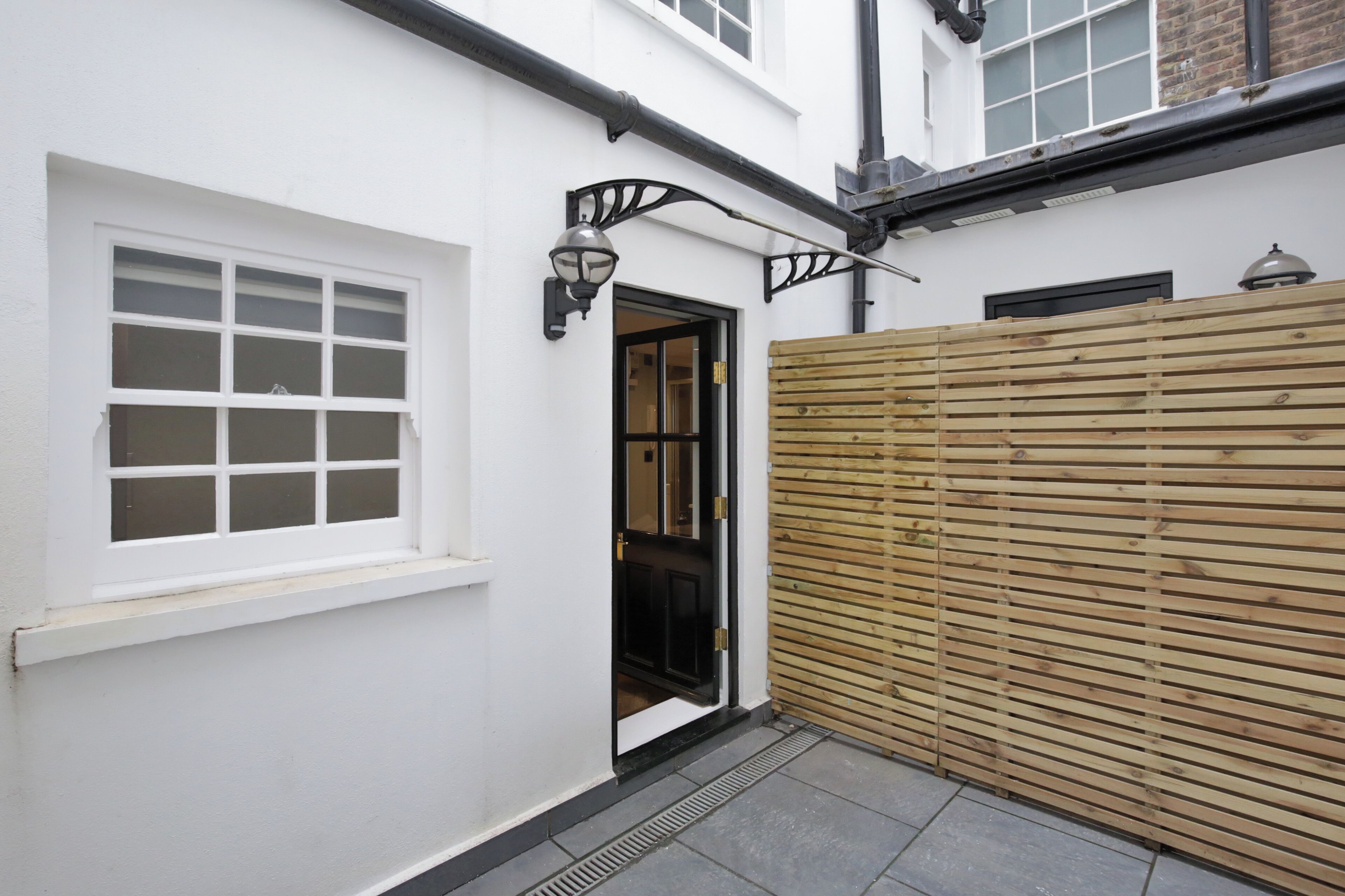 A narrow alleyway with a white building, a wooden fence, and a black door.