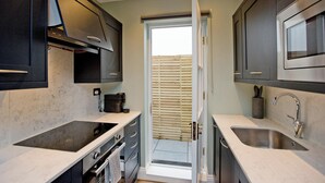 Cocina compacta con armarios oscuros, horno empotrado, un lavamanos y una ventana con persianas.