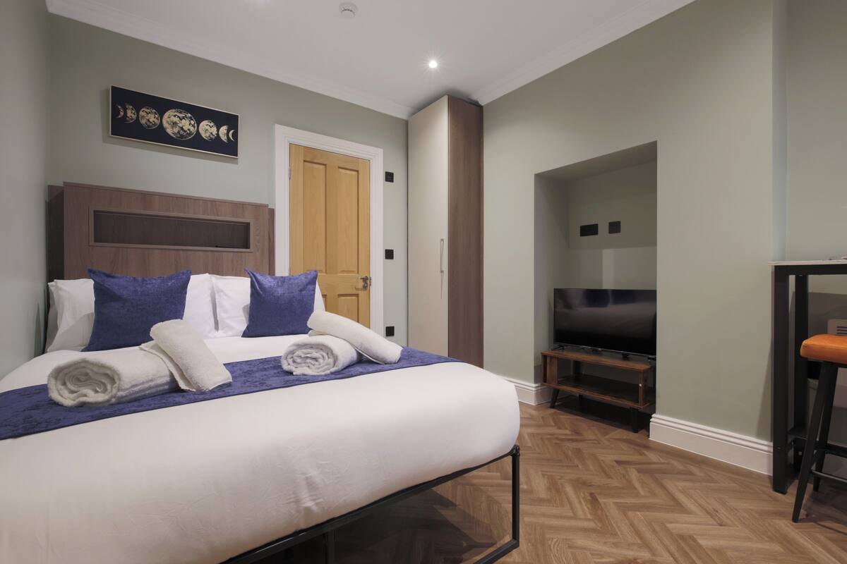 A neatly made bed with white and blue bedding, a wooden headboard, and a wall-mounted artwork depicting lunar phases.