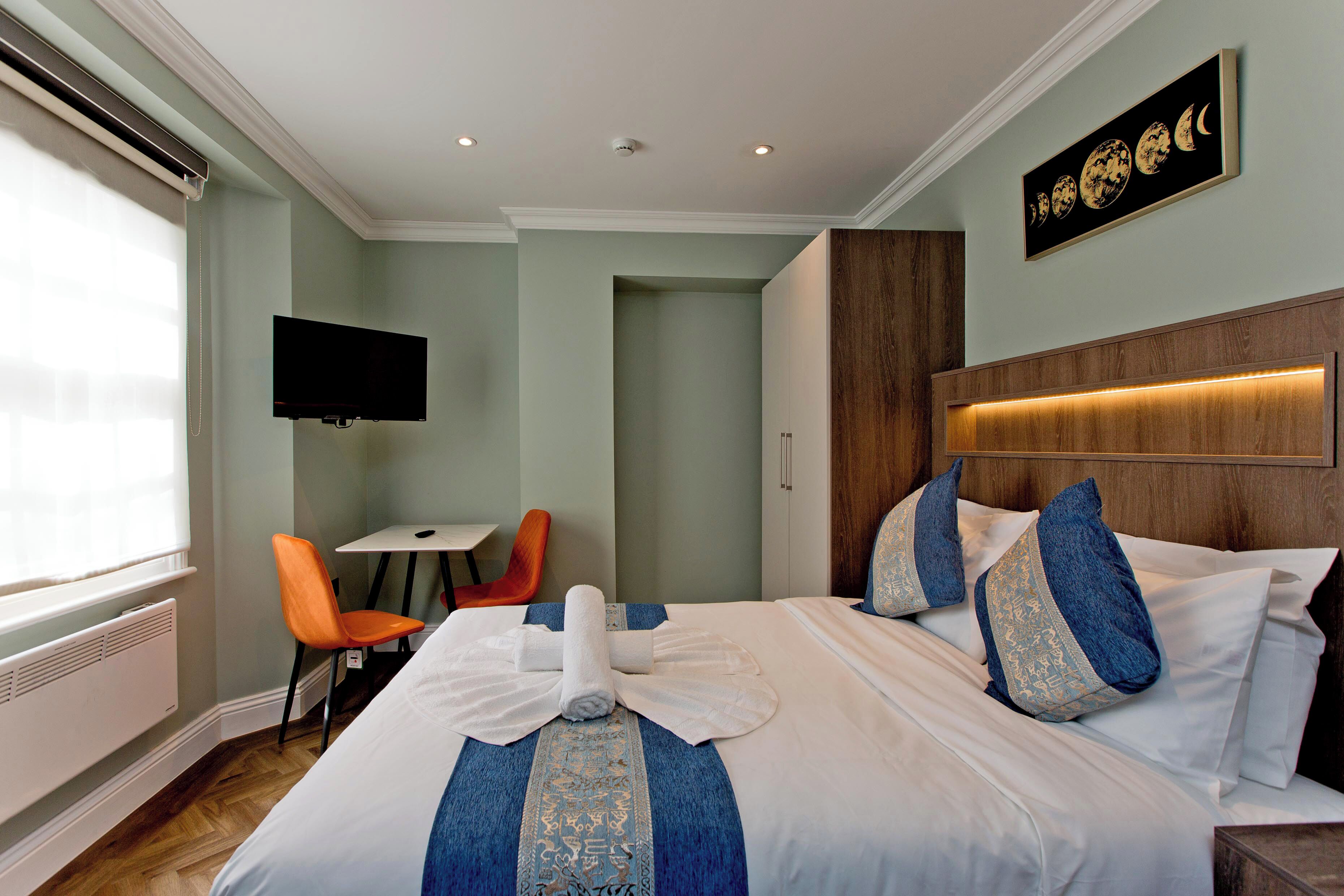 A hotel room with a bed, a television mounted on the wall, a small table, and two chairs.