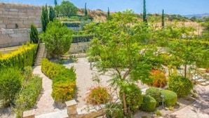 A landscaped garden with various shrubs and trees, a stone wall, and a clear sky. - Villa Fortuna (Polis)