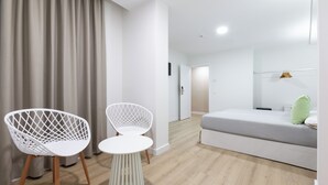 A modern hotel room with a wooden floor, a grey sofa, two white chairs, and a small white table. - Hotel Boutique HC Maga (Puerto de la Cruz)