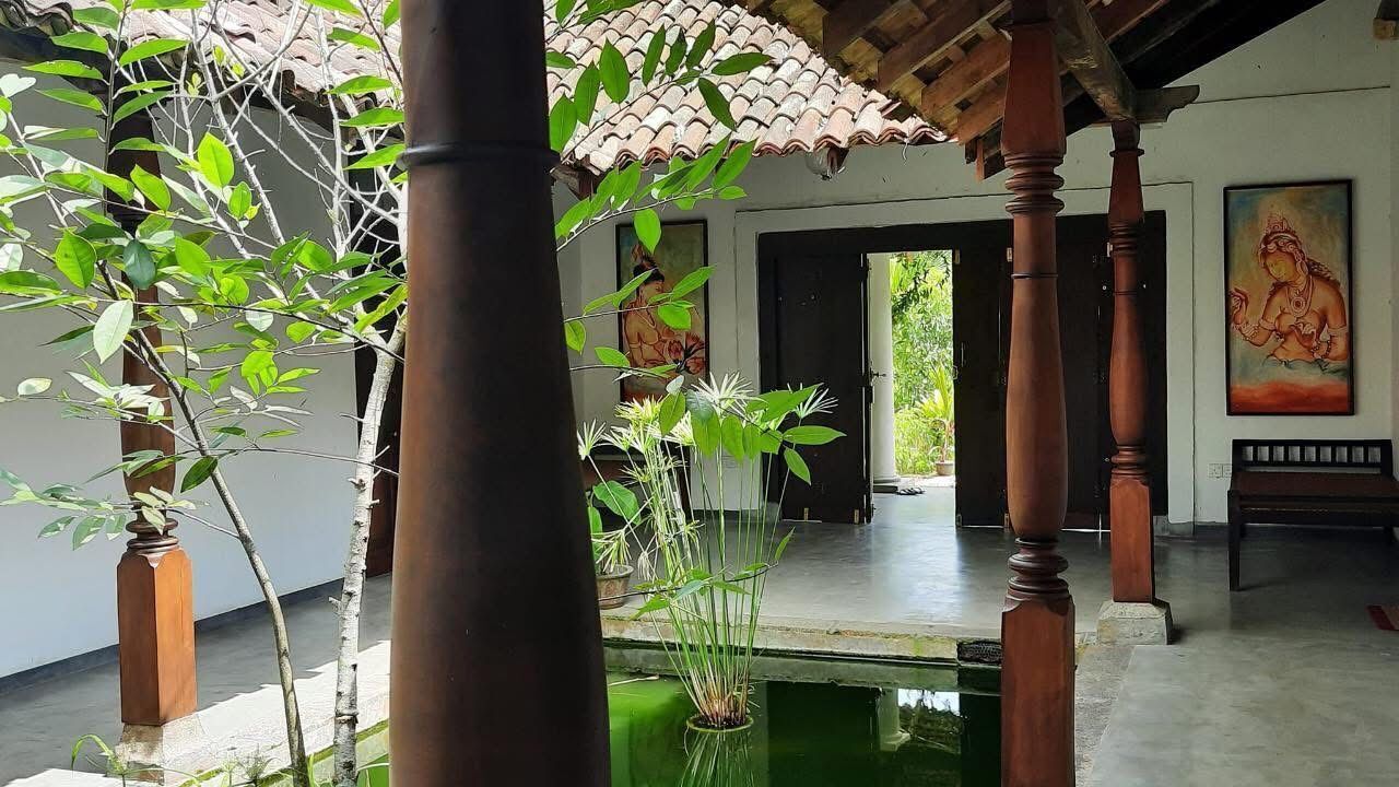 A traditional interior with a tiled ceiling, wooden pillars, a small water feature, and artwork on the walls.