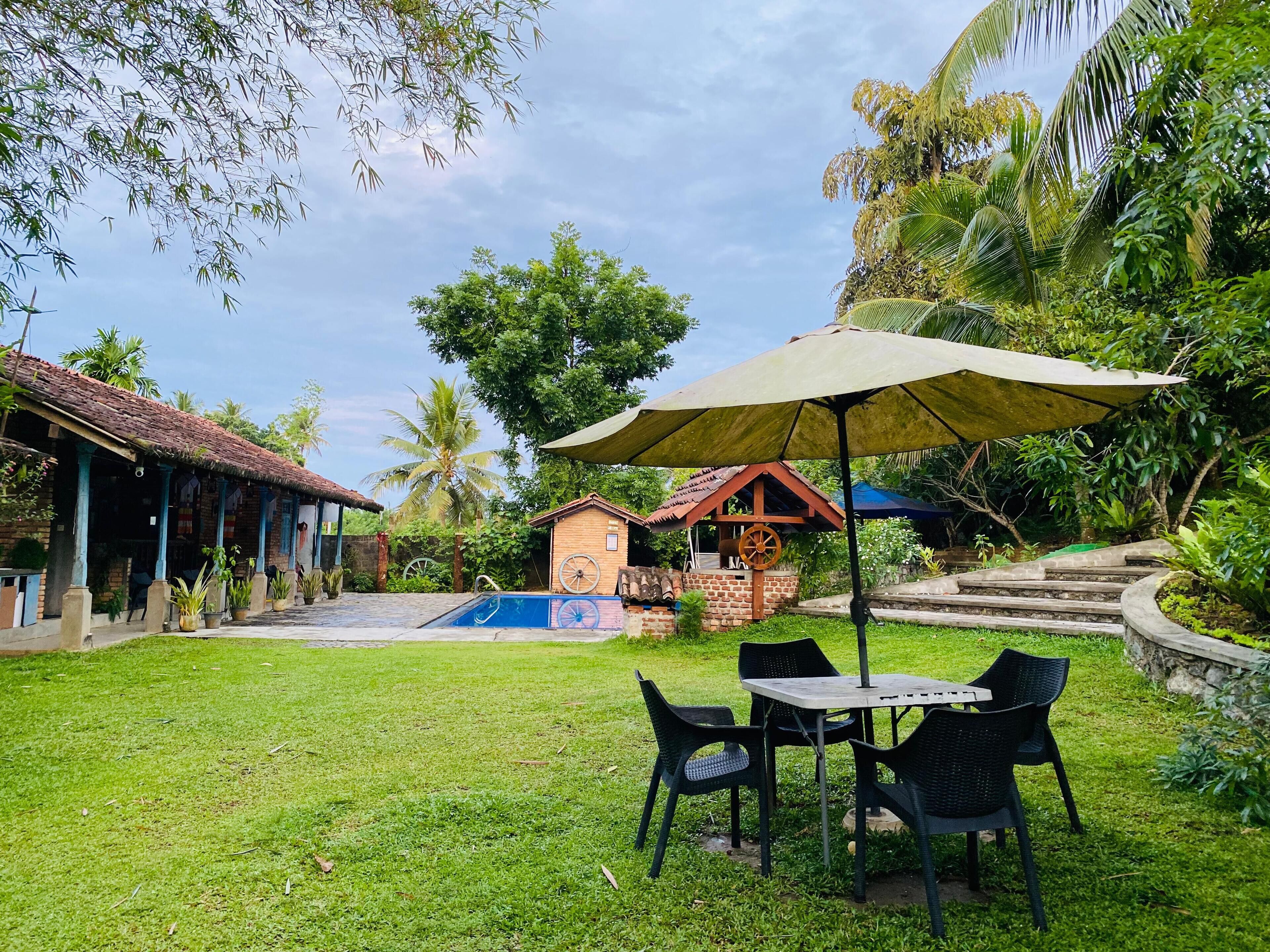 Un jardin avec une piscine, une table entourée de chaises et un espace abrité avec un parasol.