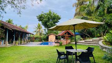 Un jardin avec une piscine, une table entourée de chaises et un espace abrité avec un parasol.