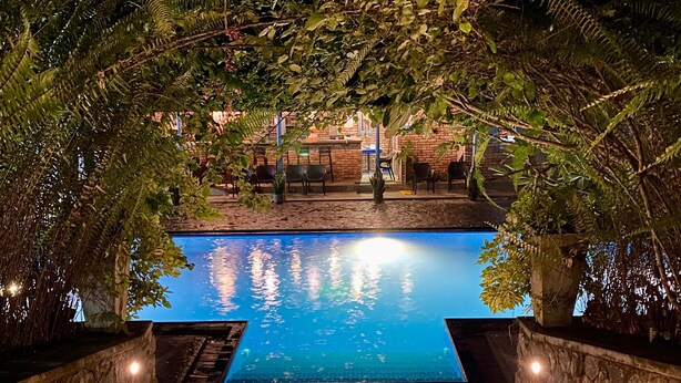 A nighttime view of a swimming pool surrounded by lush greenery and stone walls. - The Nature Palace Villa (Uragasmanhandiya)