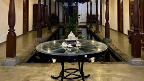 A covered outdoor area with a central glass table, wooden pillars, and a fountain. - The Nature Palace Villa (Uragasmanhandiya)