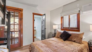 Un dormitorio con cama, ventana, puerta y una mesita de noche con lámpara.