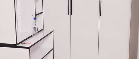 A room with a white wardrobe, a desk with a water bottle, and a marble floor.