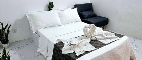 A bedroom with a bed, a small sofa, and a potted plant.