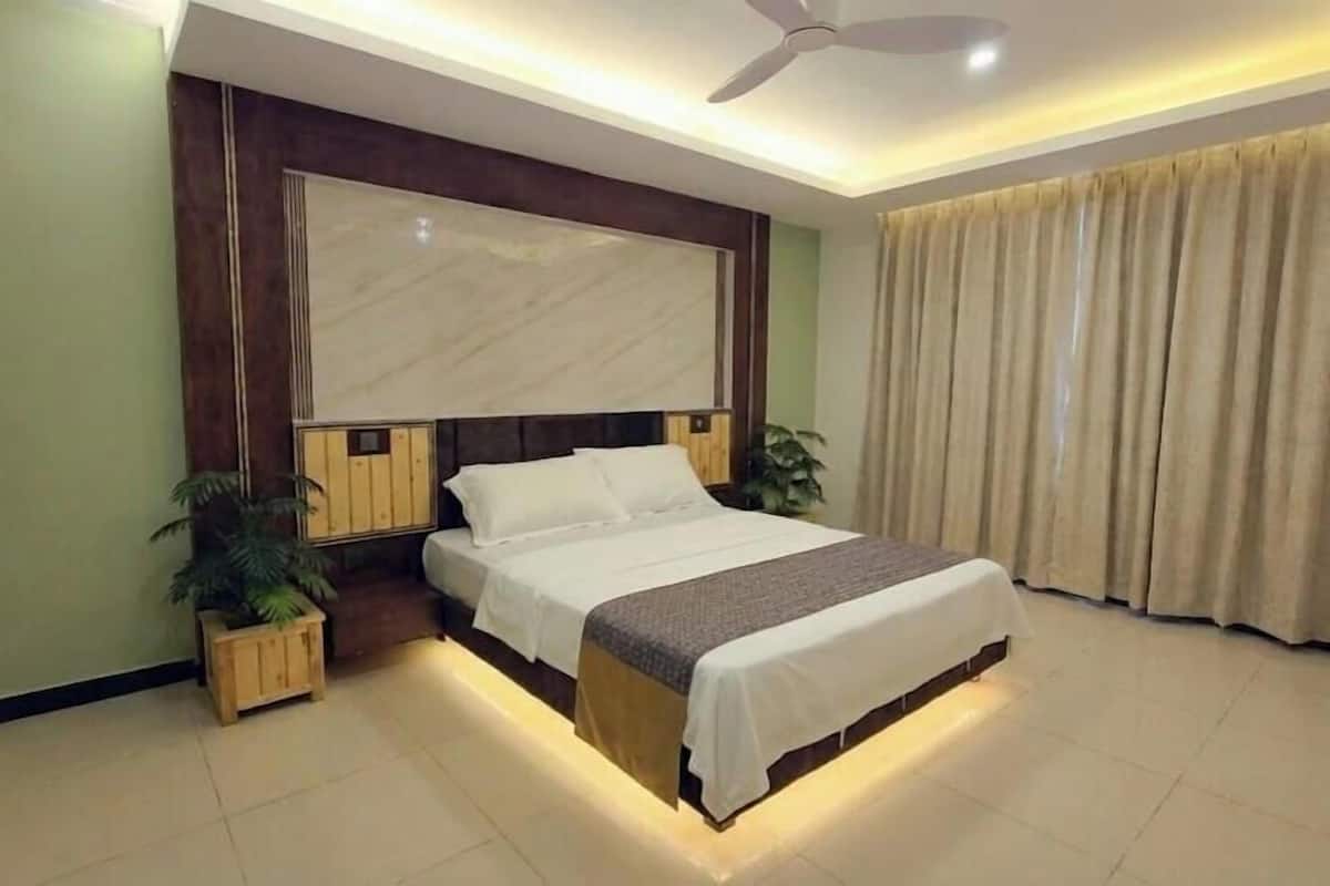 A bedroom with a bed, a ceiling fan, a window with curtains, and a small plant.