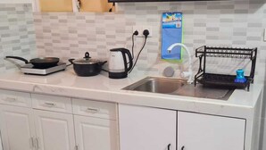 Une cuisine avec des meubles blancs, un évier, une cuisinière, une bouilloire et un égouttoir à vaisselle.