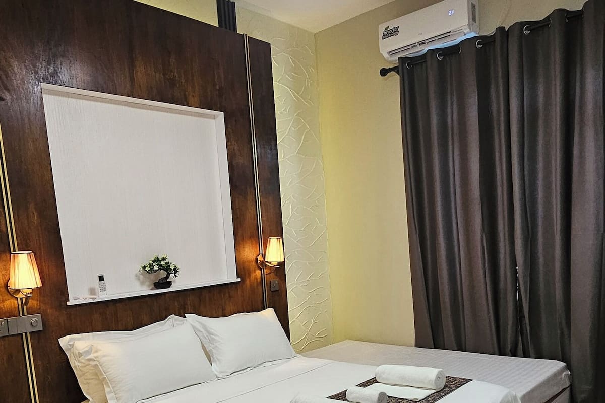 Ein Hotelzimmer mit Bett, Nachttischlampen, Deckenventilator, Klimaanlage und einem Fenster mit Vorhängen.