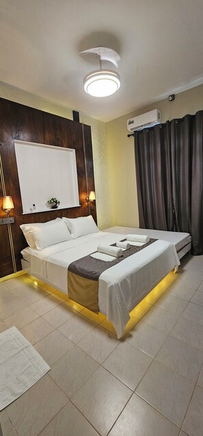 A hotel room with a bed, bedside lamps, a ceiling fan, an air conditioning unit, and a window with curtains. - Blue Haven Retreat (Thulusdhoo Island)