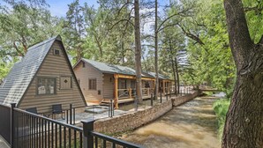 A log cabin-style building with a porch and a stone wall alongside a river.