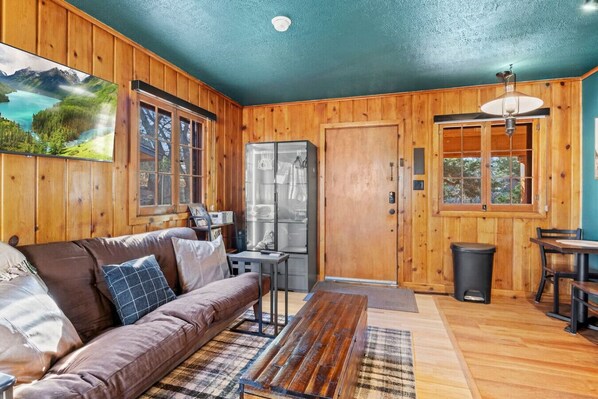 A cozy cabin interior with a wooden interior, a sofa, a dining table, and a refrigerator.