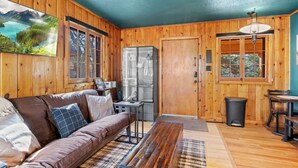 A cozy cabin interior with a wooden interior, a sofa, a dining table, and a refrigerator. - Timber Lodge Cabin #31 (Colorado Springs)