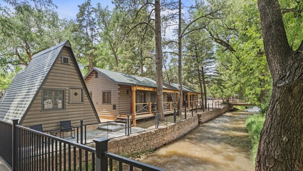 A log cabin-style building with a porch and a stone wall alongside a river. - Timber Lodge Cabin #5 (Colorado Springs)
